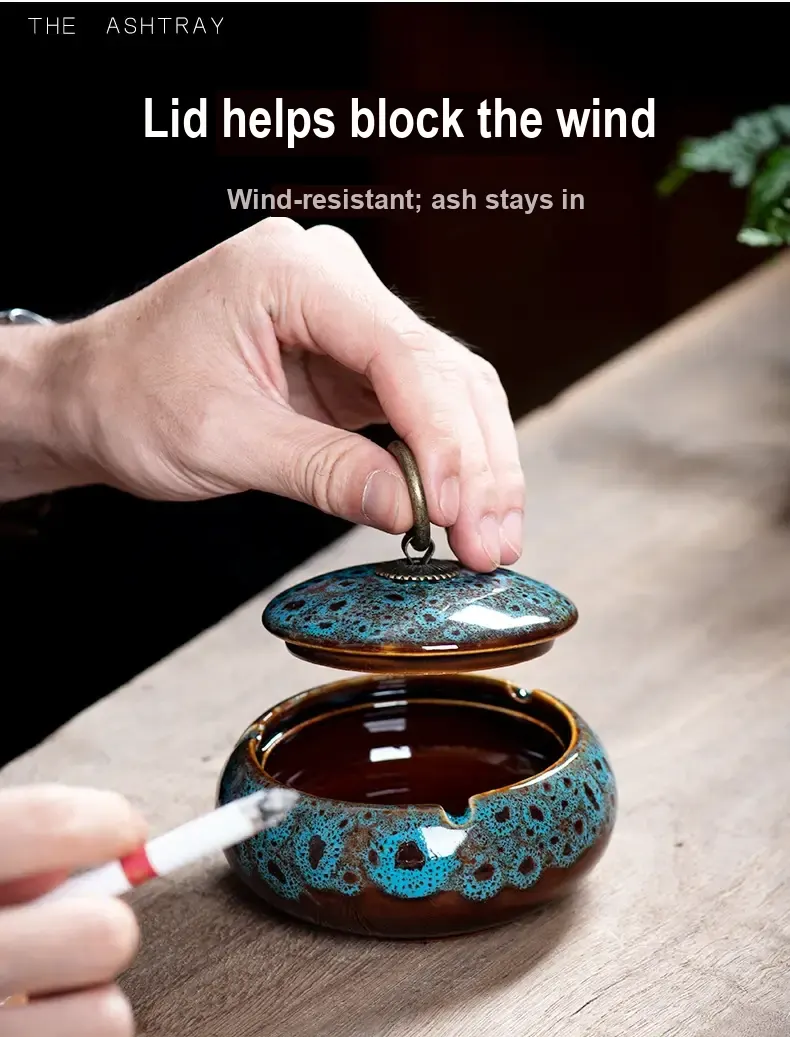 A hand lifts the ring-handled lid from a blue-speckled ceramic ashtray.