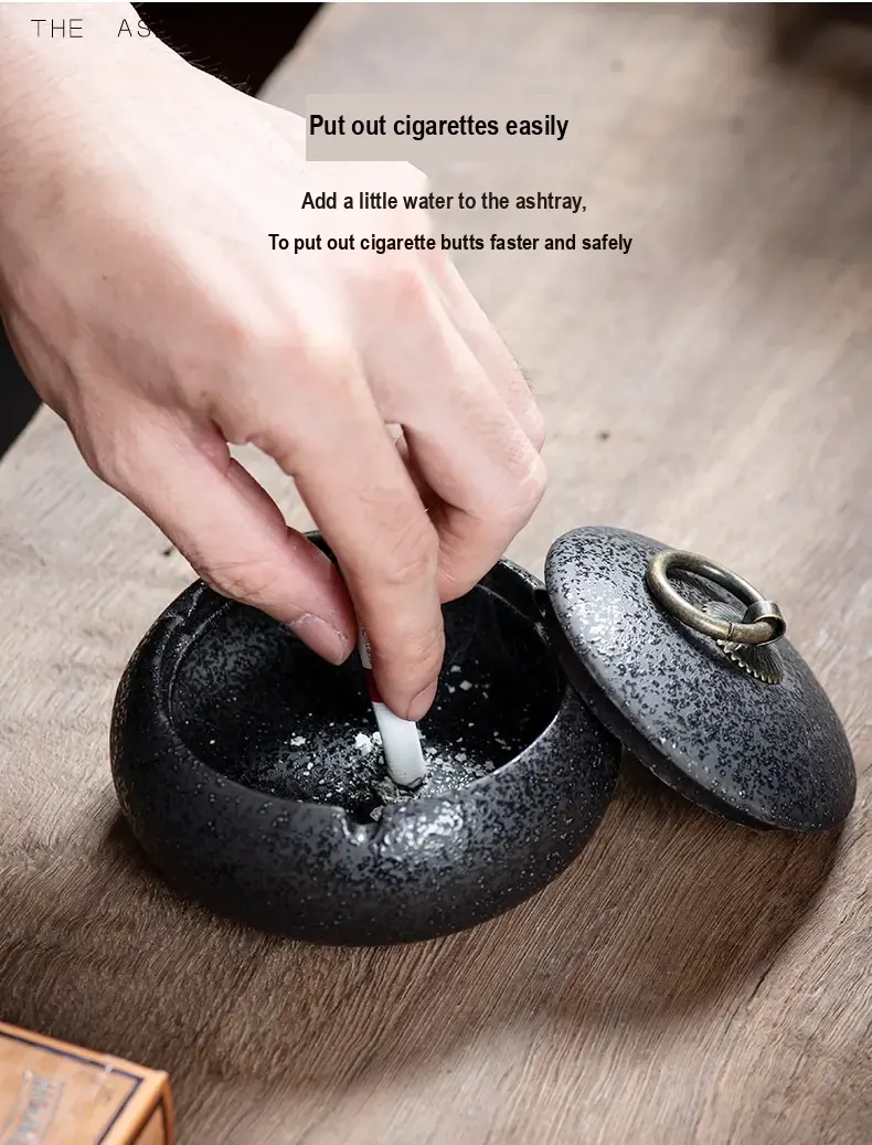 A cigarette being extinguished in a dark ceramic ashtray.